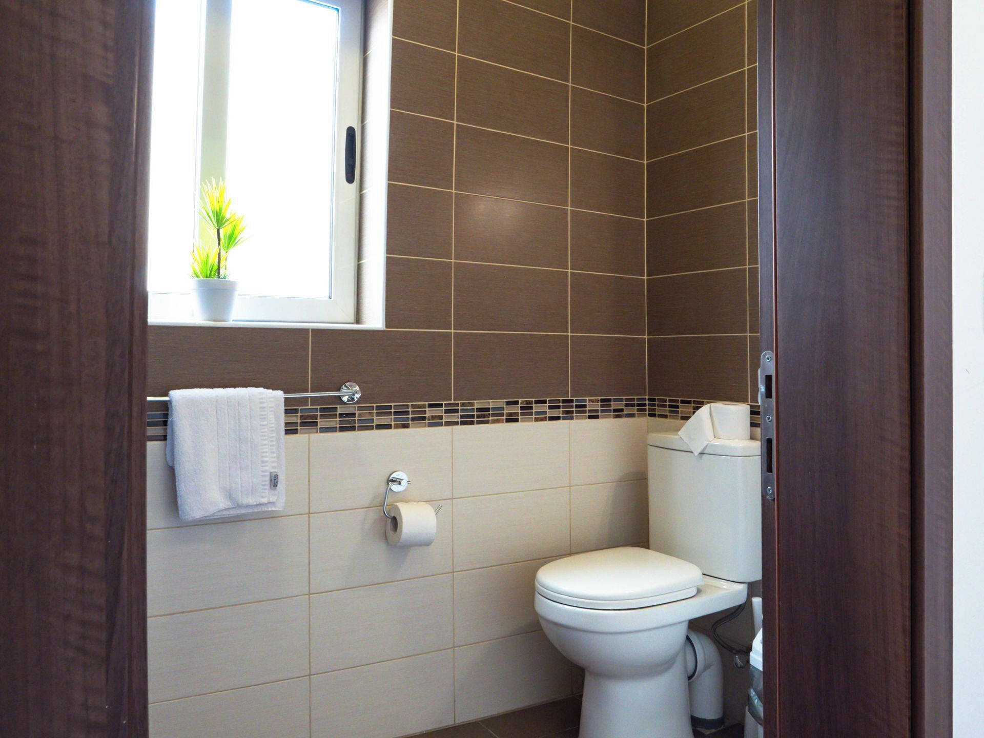 A bathroom with a toilet, a towel rack, and a window with a plant.
