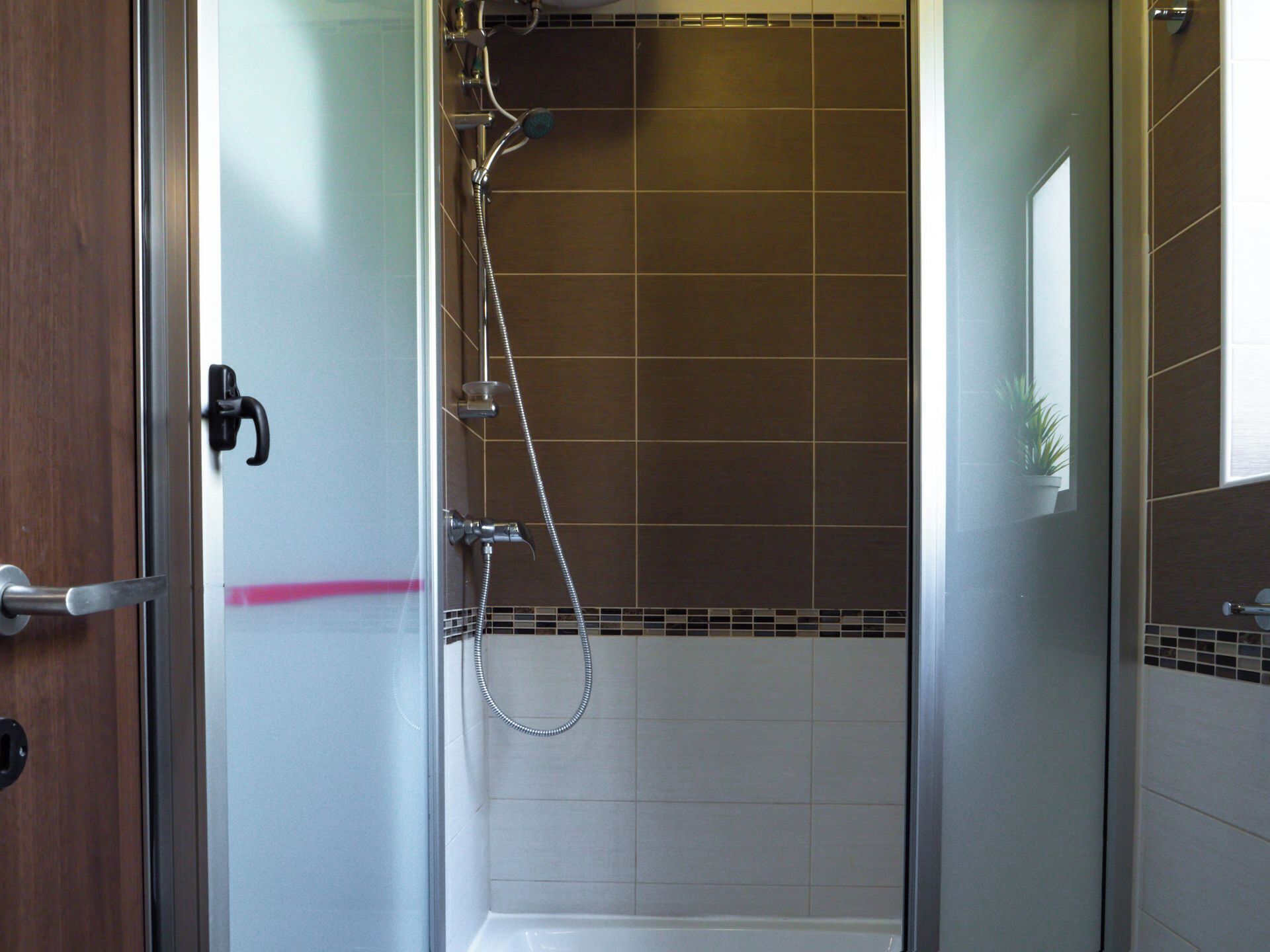 A walk-in shower with a glass door, a handheld showerhead, and a handheld showerhead with a flexible hose.