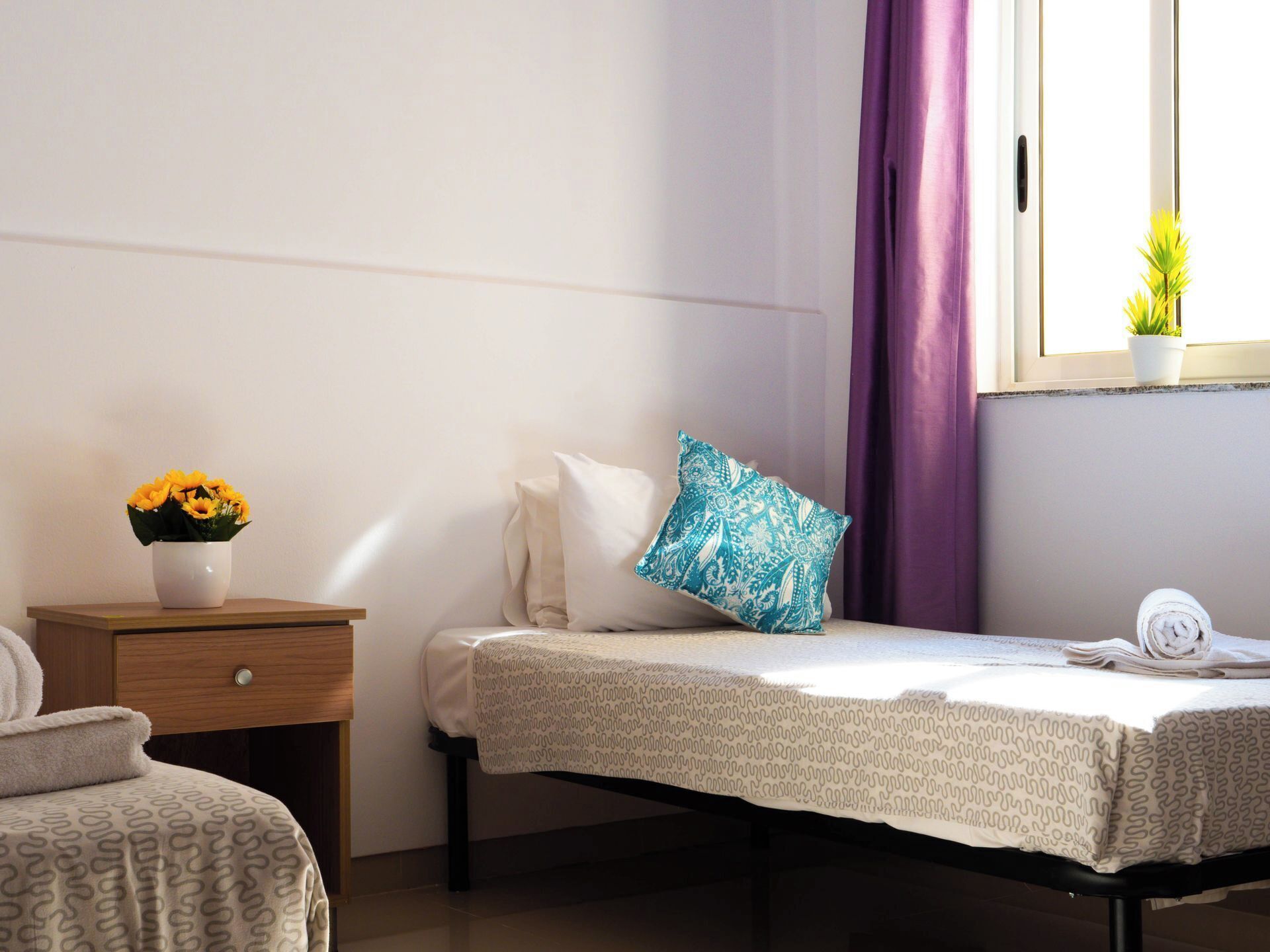 A neatly arranged bedroom with a bed, bedside table, and a window with a plant.