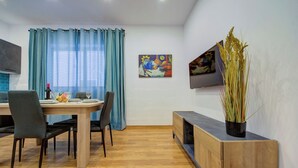 A modern dining area with a wooden table, grey upholstered chairs, and a blue curtain. - Charming Sliema Apartment Off the Ferries Seafront (Sliema)