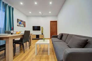 Uma sala de estar moderna com um sofá cinzento, uma mesa de jantar com cadeiras, uma televisão de tela plana e um quadro na parede.