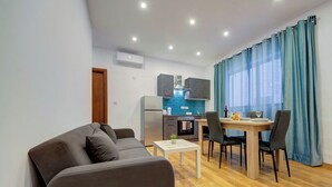 A modern living room with a sofa, a dining table with chairs, a kitchen area with a fridge, oven, and blue backsplash. - Charming Sliema Apartment Off the Ferries Seafront (Sliema)