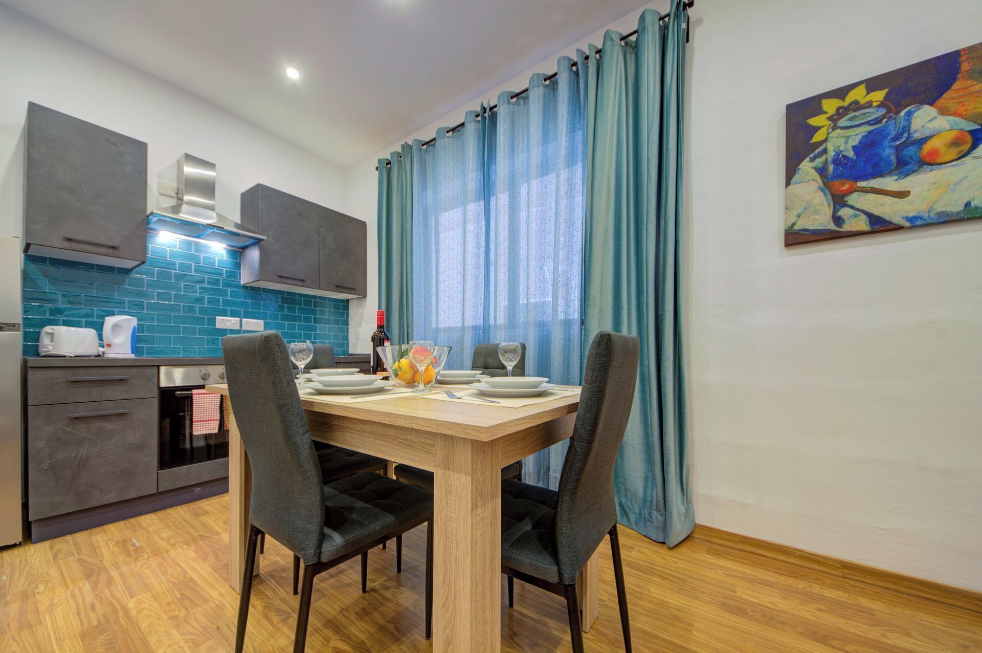 Una cocina moderna con azulejos azules, una mesa de comedor preparada para cuatro personas y un cuadro en la pared.