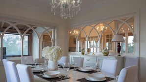 A dining area with a round table set for four, white chairs, a vase of flowers, and a chandelier. - Villa Alexandra: Sea Views, Pool, Jacuzzi & Sauna (Mellieha)