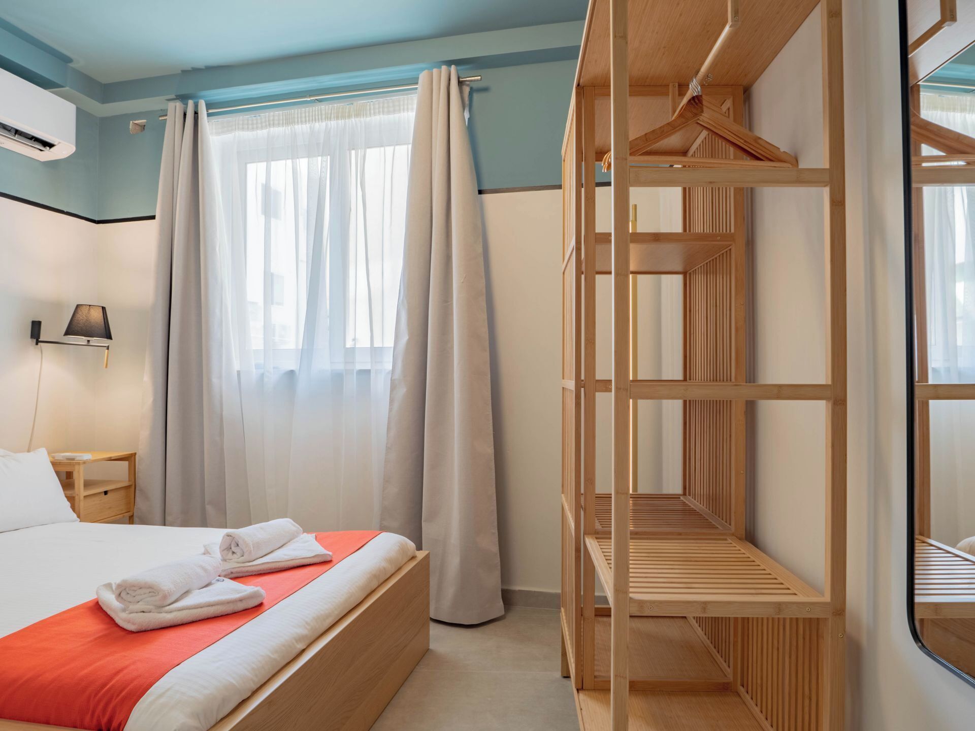 A hotel room with a bed, a wooden bunk bed, a nightstand, a lamp, and a window with curtains.