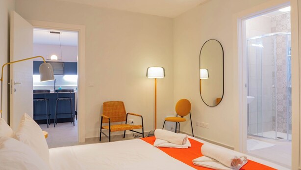 A hotel room with a bed, two chairs, a mirror, and a shower area. - Lovely Contemporary Apartment Off St. Julian's (St. Julian's)