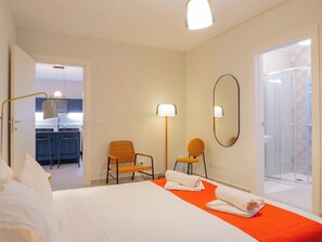 Une chambre d’hôtel comprenant un lit, deux chaises, un miroir et un espace douche.