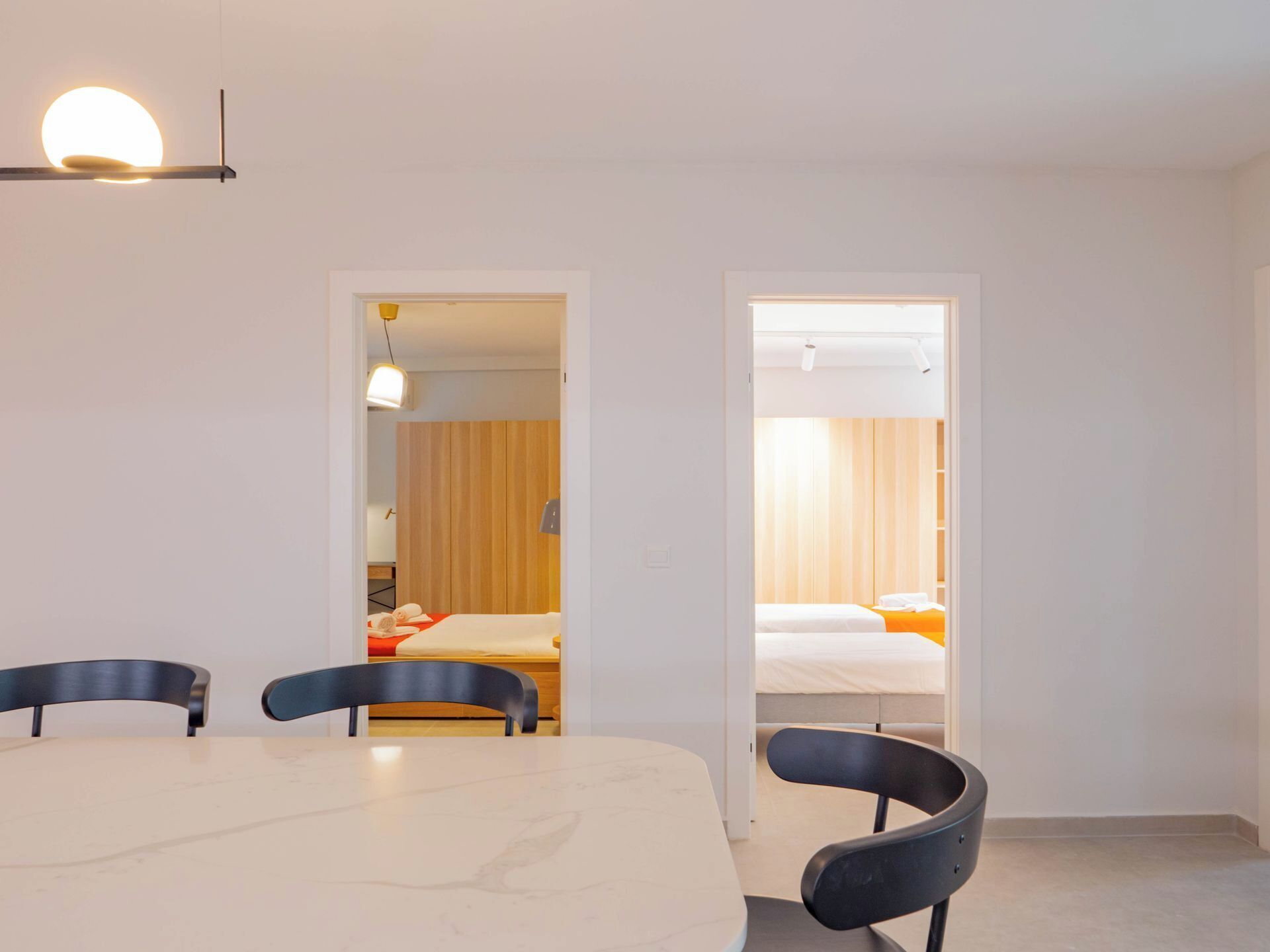 A modern hotel room with a dining area, a bed with orange bedding, and a wooden panel wall.