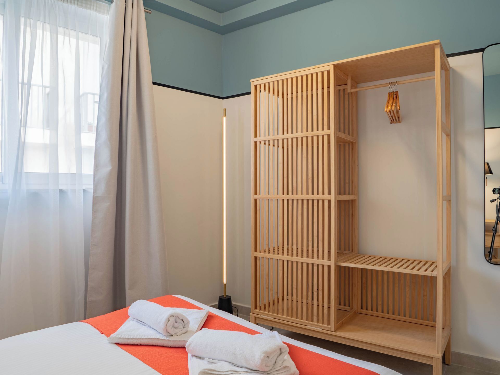 Una habitación de hotel con cama, armario de madera y ventana con cortinas.