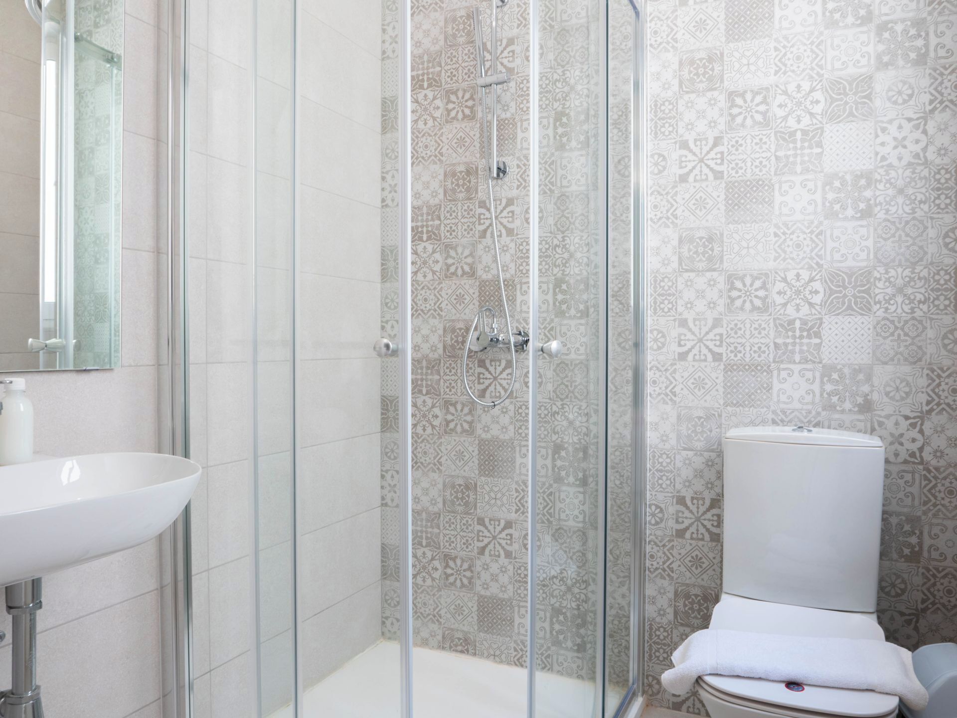 A bathroom with a glass-enclosed shower, a white sink, and patterned tiles.