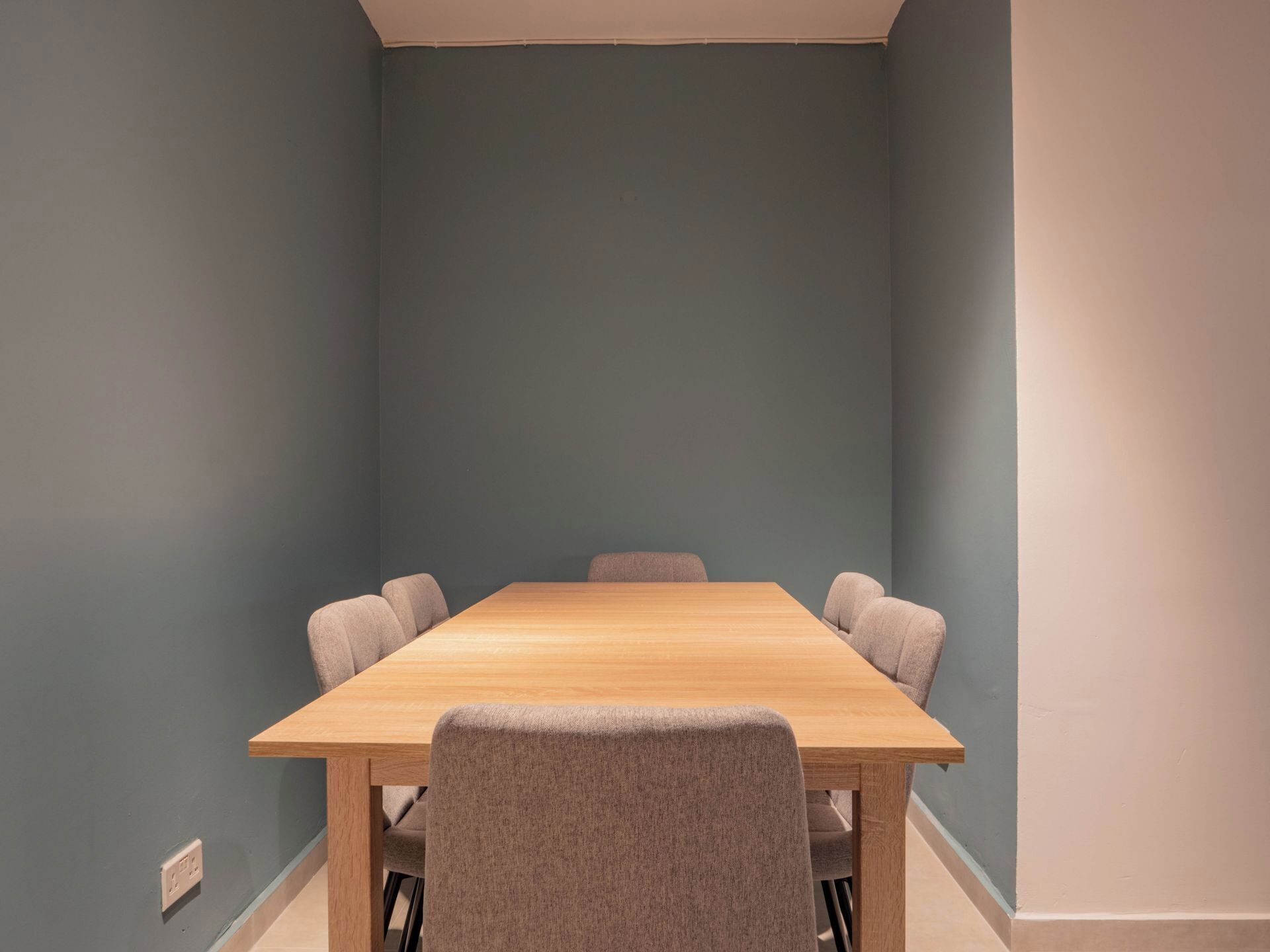 A conference room with a wooden table and six grey chairs.