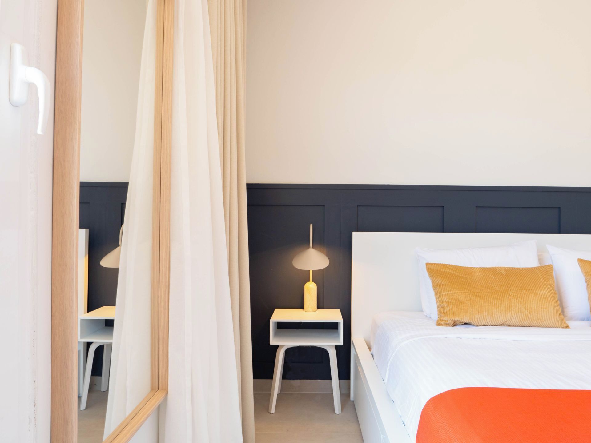 Une chambre d’hôtel avec un lit, une table de chevet avec une lampe, une chaise et un miroir.