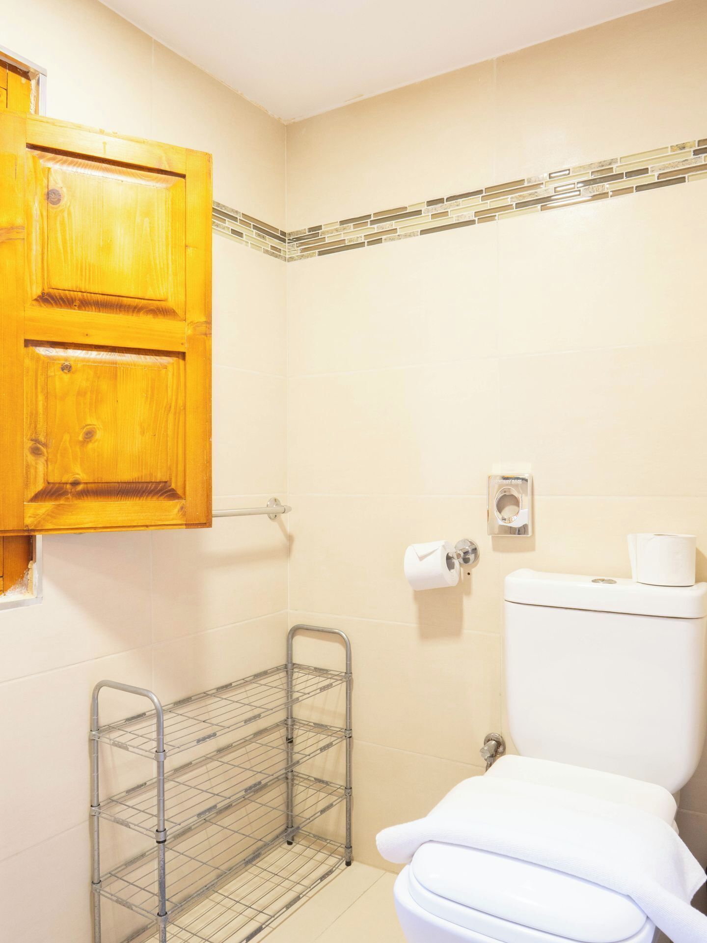 A bathroom with a wooden cabinet, a toilet, a metal shelf, and a wall-mounted toilet paper holder.