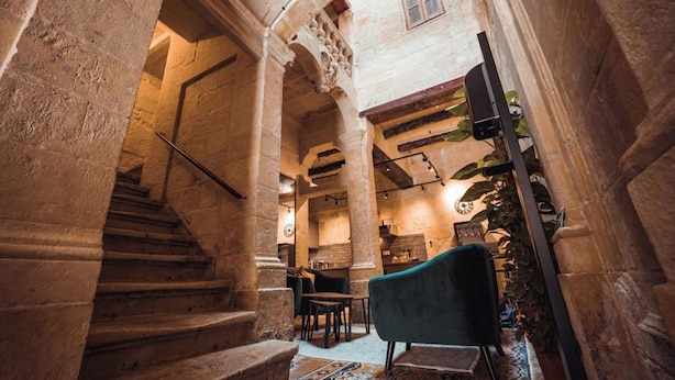 A stone staircase leading to a room with a green chair, a table, and a potted plant. - Palazzino Valentina Valletta (Valletta)