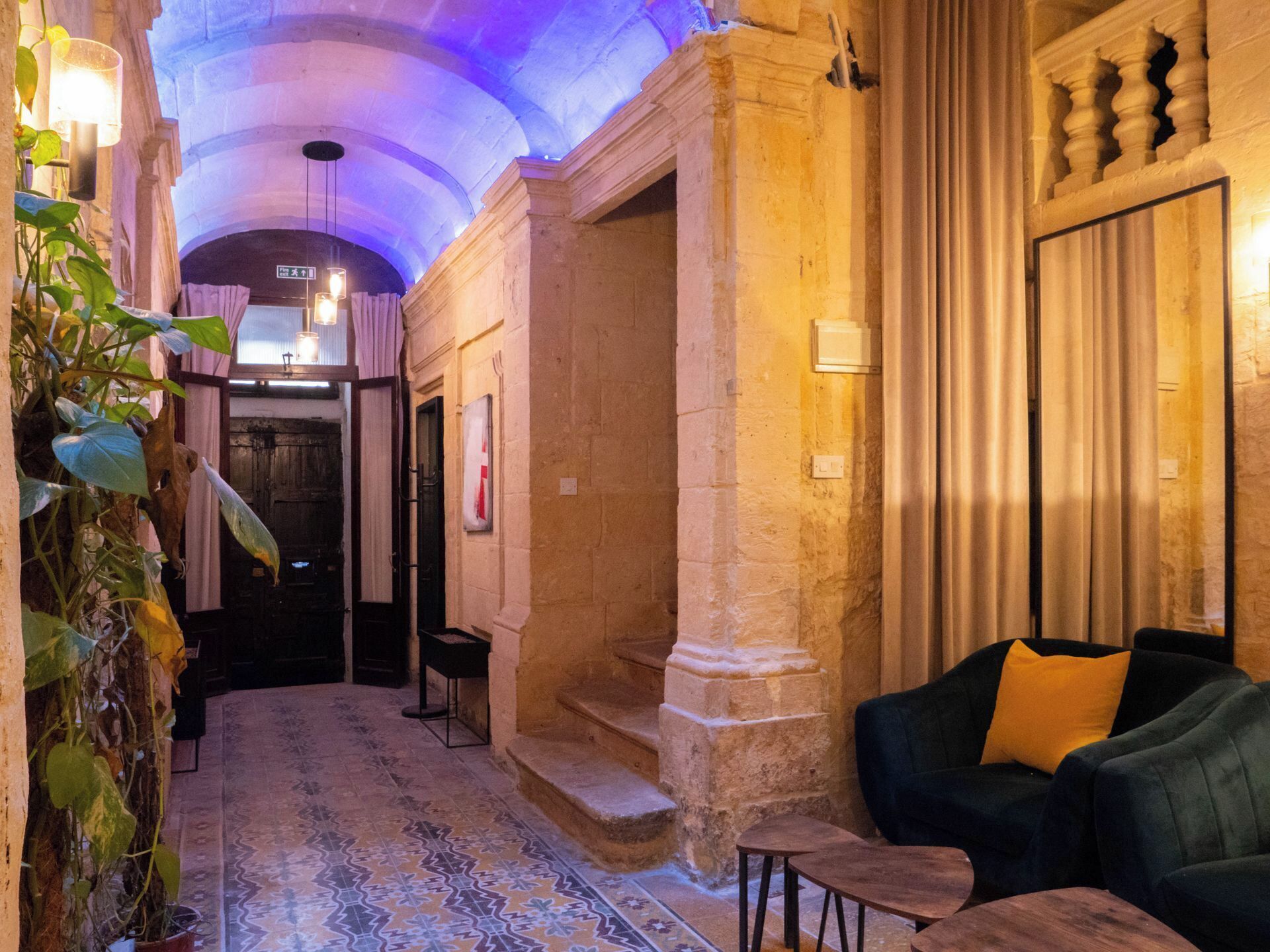 A corridor with a tiled floor, a staircase, a seating area with a sofa and a small table, and a door leading to another room.