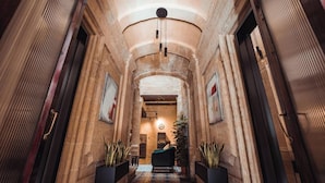 A corridor with stone walls, a chandelier, and potted plants. - Palazzino Valentina Valletta (Valletta)