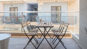 Een balkon met een tafel en vier stoelen, met uitzicht op een woonwijk met gebouwen en een hek.