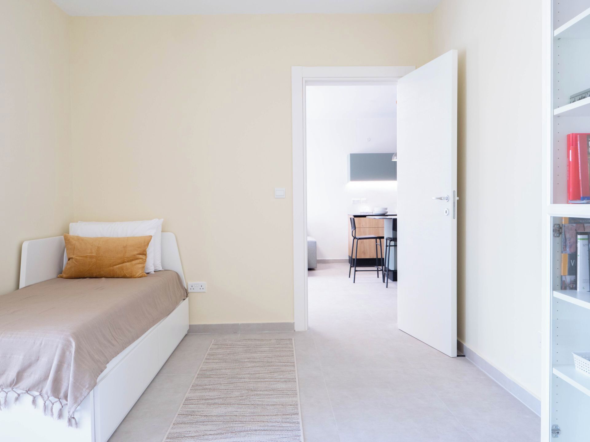 A bedroom with a bed, a bedside table, a nightstand, a small desk with a chair, and a bookshelf.