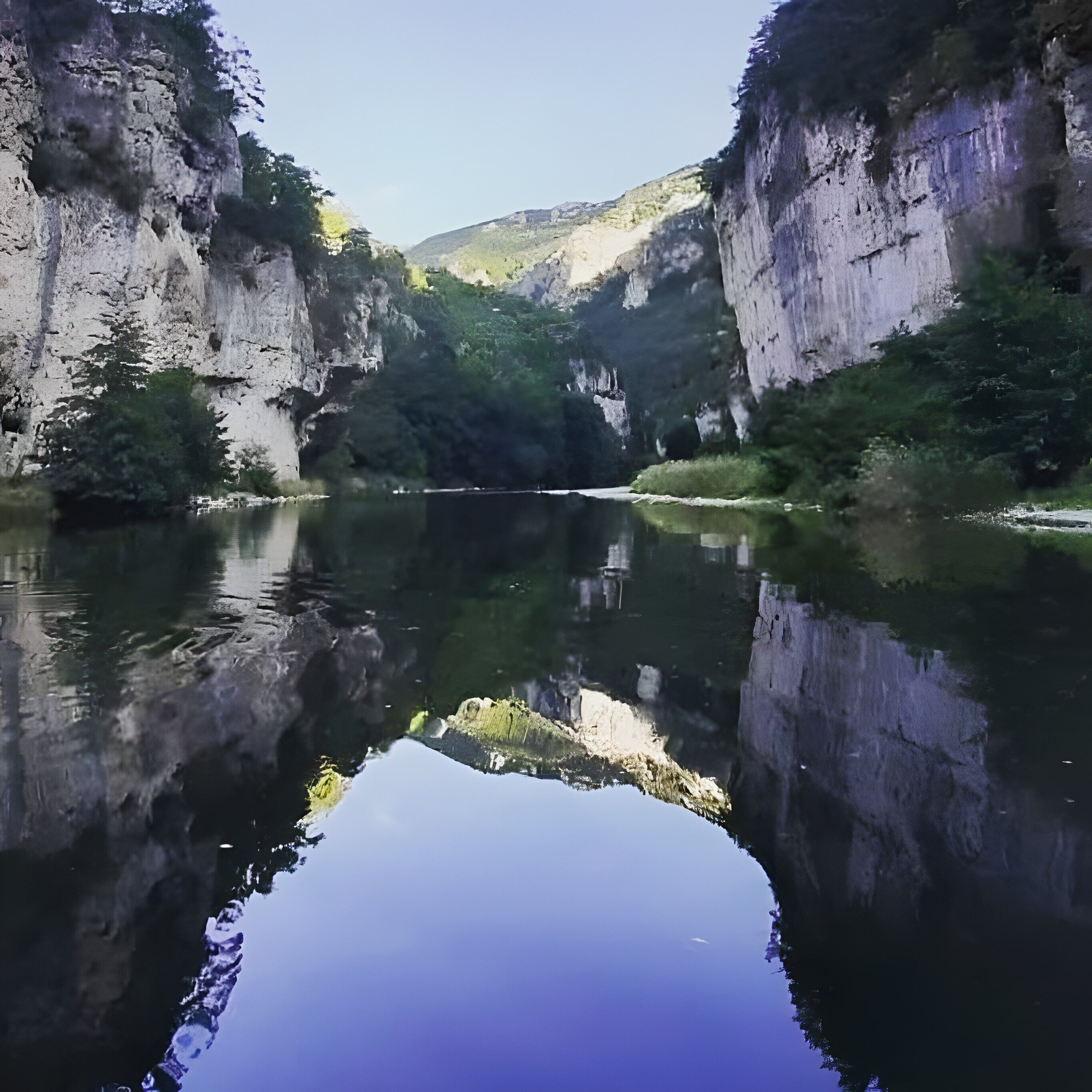 Een rustige rivierkloof met kliffen aan beide zijden en een heldere weerspiegeling in het water.