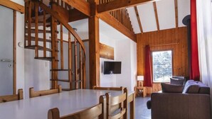 A wooden interior with a dining table, chairs, a sofa, a TV, and a window with curtains. - Les Bouviers (Saint-Paul-le-Froid)