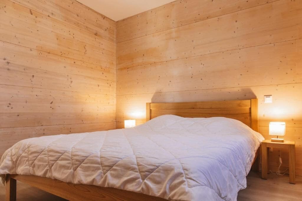 A wooden-paneled room with a bed, two bedside lamps, and a wooden bench.