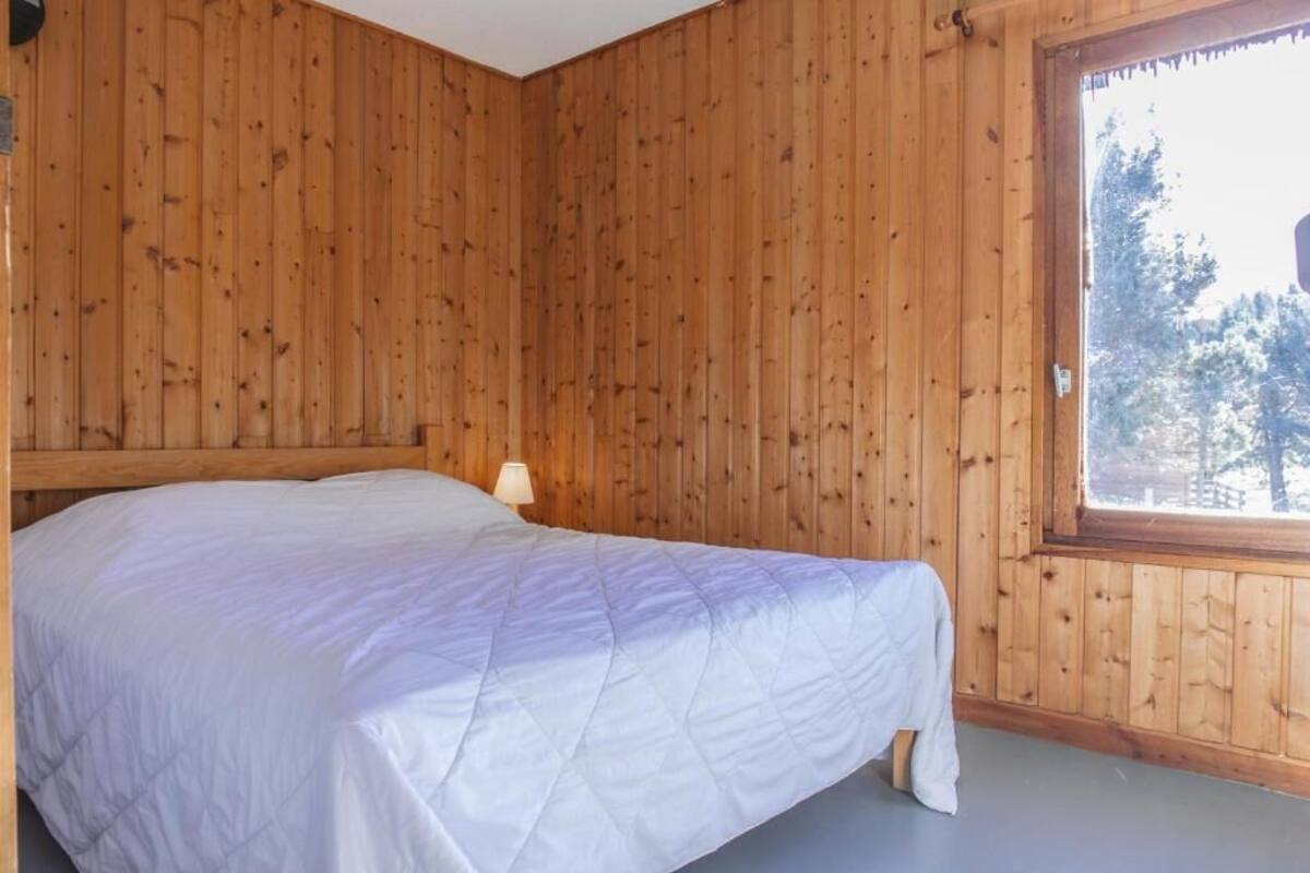 A wooden-paneled room with a bed, a window, and a door.