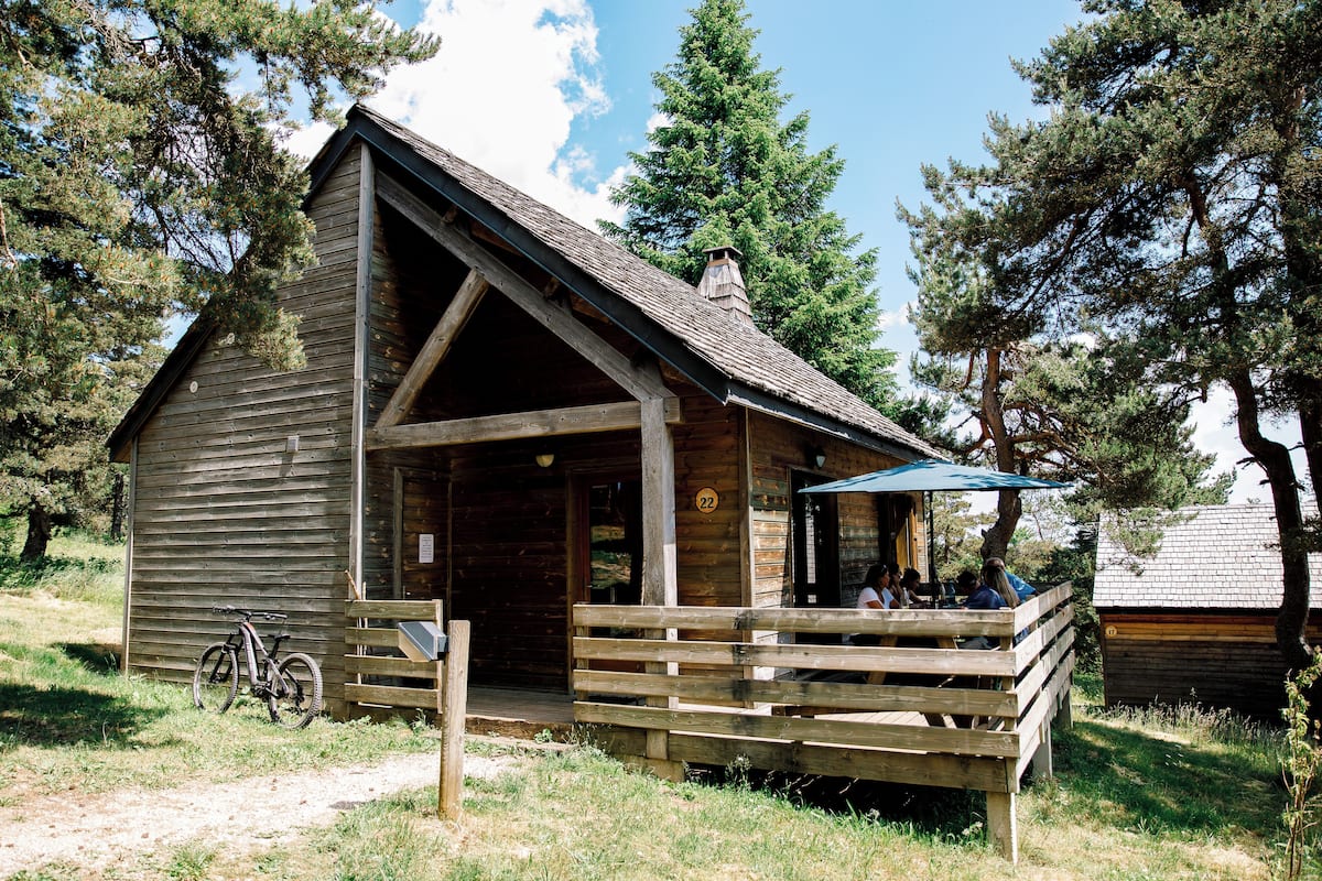 A rustic wooden cabin with a porch, a bicycle parked outside, and a clear sky.