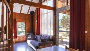 A cozy cabin interior with a wooden ceiling, a sofa, a dining table, and large windows. - Les Bouviers (Saint-Paul-le-Froid)