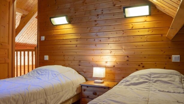 Une chambre dans un chalet en bois, avec deux lits, une table de chevet avec une lampe et un plafond en pente.