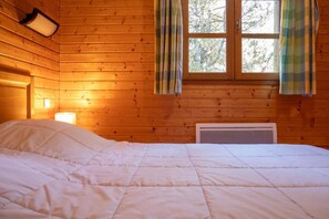 Una habitación de cabaña de madera con una cama, una ventana con cortinas y un calentador fijado a la pared.