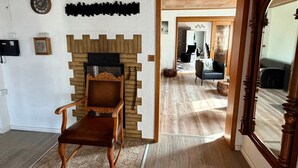 Ein Zimmer mit einem Holzsessel, einem Kamin, einer Uhr und einem Durchgang zu einem weiteren Raum.