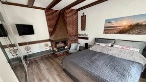 Ein Schlafzimmer mit Kamin, einem Bett mit gesteppter Decke, einem Wand-Fernseher und einem Bild an der Wand.