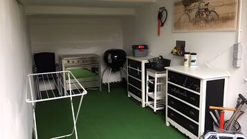 A compact kitchen with a gas stove, drying rack, storage cabinets, and a bicycle painting on the wall.