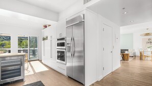 A modern kitchen with stainless steel appliances, a dining area with a wooden table, and a view of greenery outside. - Laurel Ridge: Elevated Canyon Escape with Spa-Like Living & Style (Hollywood Hills)
