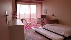 Um quarto com cama, escrivaninha, cadeira e uma mesinha.