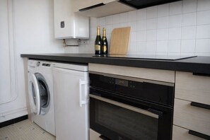 A compact kitchen with a washing machine, a microwave, and a built-in oven. - City center apartment in Les Sables-d’Olonne – sleeps 6 (Les Sables-d´Olonne)