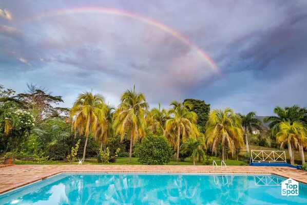 A swimming pool with a view of palm trees and a rainbow in the sky.