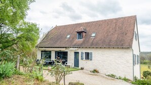 A two-story stone house with a sloped roof, a covered porch with outdoor seating, and a gravel driveway. - Holiday Home “Gite Chez Léontine” with Private Terrace, Wi-Fi and Air Conditioning (Lacave)