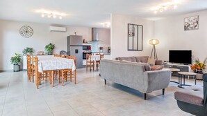 A modern living room with a sofa, TV, and dining area with chairs and a table. - Holiday Home “Gite Chez Léontine” with Private Terrace, Wi-Fi and Air Conditioning (Lacave)