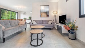 A modern living room with a sofa, two round tables, a TV, and a potted plant. - Holiday Home “Gite Chez Léontine” with Private Terrace, Wi-Fi and Air Conditioning (Lacave)