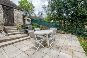 A stone building with a wooden door, a small white house, and a round table with chairs in a garden setting. - Holiday Home “La Vallée de l’Ouysse 5”: Mountain View, Wi-Fi, Air Conditioning (Lacave)