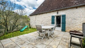 A stone building with a tiled patio, a table with chairs, and a slide.