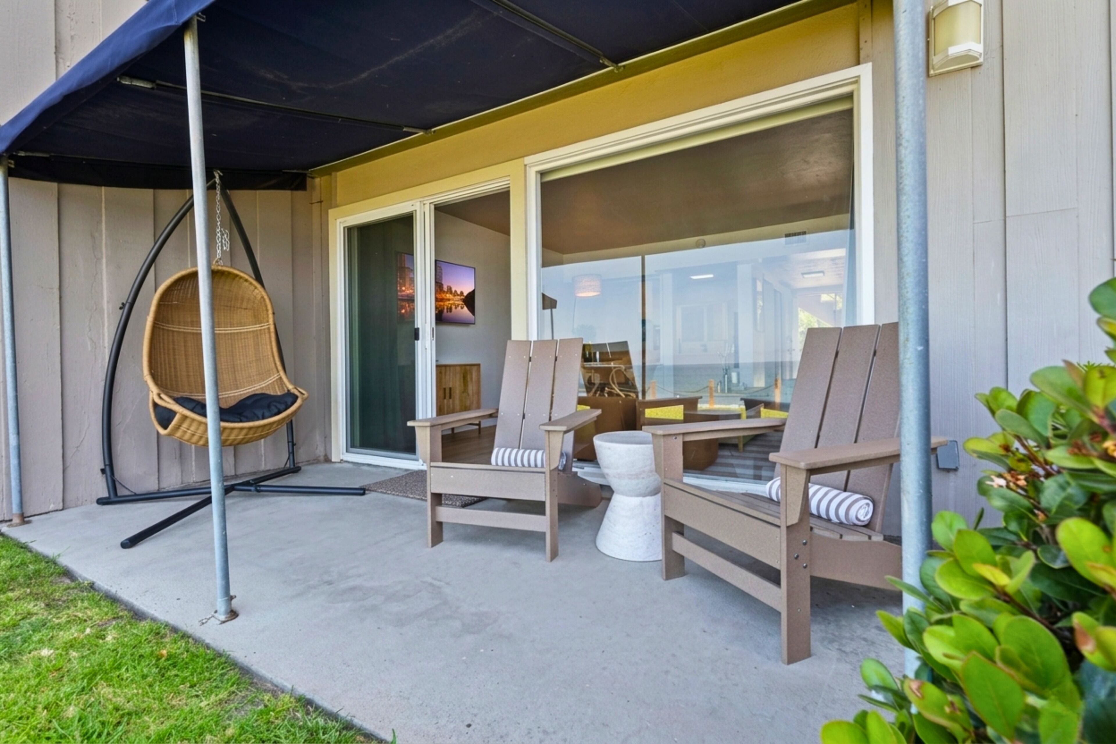Un patio con mobiliario exterior, incluyendo sillas y un sillón colgante, cerca de un edificio con amplias ventanas.