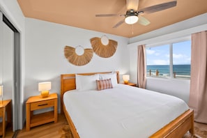 A hotel room with a bed, wooden nightstands, a ceiling fan, and a view of the ocean. - The Golden Hour - Ocean Front (San Diego)