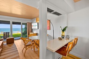 A room with a view of the ocean, a dining area with wicker chairs, a television, and a plant on the table. - The Golden Hour - Ocean Front (San Diego)
