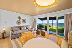 A living room with a sofa, coffee table, wicker chairs, and a view of the ocean through large sliding doors. - The Golden Hour - Ocean Front (San Diego)