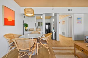 A modern interior with a dining area featuring wicker chairs and a round table, a kitchen with stainless steel appliances, and a living area with a sofa and coffee table. - The Golden Hour - Ocean Front (San Diego)