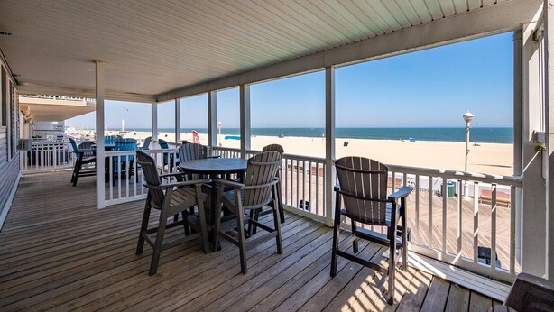 A covered deck with a table and chairs, overlooking a beach. - Columbus Villa 107 - 3 bedroom on the boardwalk with great beach and ocean views~ (Ocean City)
