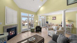 A living room with a fireplace, a dining area, and a view through glass doors. - Pelican Perch - 3 bed/ den on water with boat dock and outdoor pool - 36th St area sleeps 10 (Ocean City)