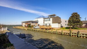 A waterfront property with a dock, a white building with a blue roof, and a tree. - Pelican Perch - 3 bed/ den on water with boat dock and outdoor pool - 36th St area sleeps 10 (Ocean City)